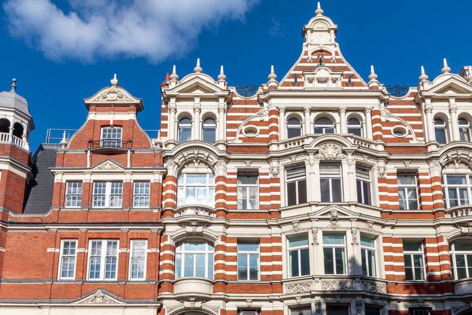 A detailed exterior view of a historic listed building in Kennington, showcasing a brick facade accented by ornate white wooden window frames and decorative architectural elements. The building featur